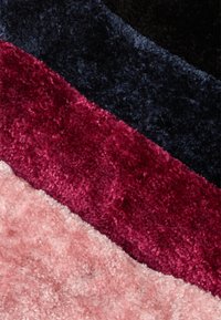 Tapete de pelúcia multicolorido com riscas horizontais em tons de rosa, burgundy, azul-escuro e preto, com uma textura suave e felpuda.