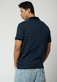 Polo shirt blu navy a maniche corte, con un motivo decorativo di piccole forme geometriche. Colletto e polsini a costine, vestibilità comoda. Pantaloni corti in denim.