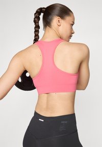 Ružičasti atletski crop top s racerback dizajnom, uparen s crnim tajicama visokog struka. Značajni detalji uključuju akcentne šavove i oznaku logotipa.