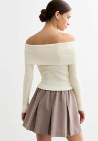 Geribbelde off-shoulder top in crème, met lange mouwen en een getailleerd ontwerp. Gecombineerd met een geplisseerde taupe rok, die zachte texturen benadrukt.
