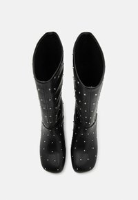 Mustad mustekad kõrge säärega saapad, mis on valmistatud siledast nahast, hõbedaste nööbiga ühtlaselt kaunistatud pealmises osas ning ümarate varvaste disainiga.