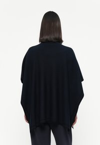 Poncho navy in tessuto morbido, caratterizzato da un design ampio e drappeggiato con scollo rotondo e senza chiusure. Texture liscia, stile minimalista.