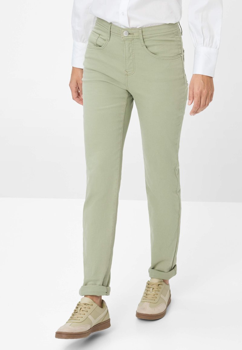 Hellgrüne Baumwollhose mit schmaler Passform, ausgestattet mit fünf Taschen und aufgerollten Bündchen, kombiniert mit beigen Sneakers. Minimalistisches Design.