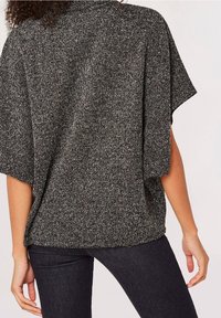 Haut en maille texturée noir et gris à manches courtes, coupe ample, décolleté large et épaules tombantes, associé à un jean foncé.