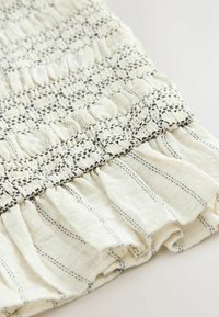 Gros plan sur un tissu blanc à rayures verticales noires, présentant un smock froncé et un détail de bordure froncée.