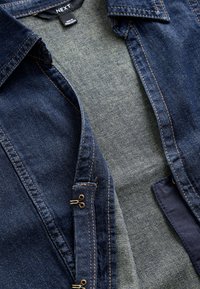 Chaqueta vaquera con acabado azul oscuro, forro interior en azul claro contrastante, costuras doradas y detalles de cremallera metálica.