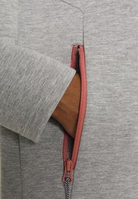 Tissu de sweat-shirt gris avec une poche zippée sur la manche, dotée d'un tirage de zip corail et d'un cordon noir et blanc contrastant.