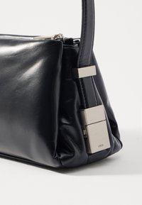 Borsa a mano in pelle nera con texture liscia, forma strutturata e un accento di hardware argentato sulla tracolla regolabile.