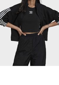 Black athletic outfit featuring a cropped top and zip-up jacket with white stripes. Textured shorts and minimalist branding on the top.