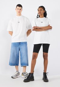 Hvide oversized t-shirts med "bell" logo, parret med blå denim culottes og sorte cykelshorts. Fodtøj inkluderer mønstrede sneakers og sorte støvler.