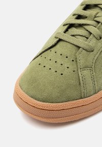 Γκρι ελιάς σουέτ αθλητικό παπούτσι με υφή καφέ ελαστική σόλα. Τρυπ�ημένη περιοχή στο μπροστινό μέρος και επίπεδα κορδόνια. Καθαρές γραμμές με μίνιμαλ σχεδίαση.