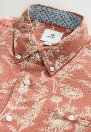 Short-sleeve shirt in coral with white floral print, textured fabric, white buttons, and a contrasting patterned inner collar. Brand label visible.