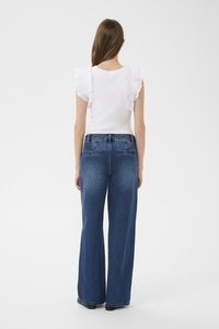 Biely žíhaný top s volánovými rukávmi v kombinácii s modrými džínsami s vysokým pásom a širokými nohavicami. Hladká textúra a klasický dizajn s piatimi vreckami.