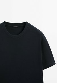 Dunkelblaues Baumwoll-T-Shirt mit kurzen Ärmeln und rundem Halsausschnitt. Glatte Textur mit einem Etikett auf der Innenseite des Halsausschnitts.