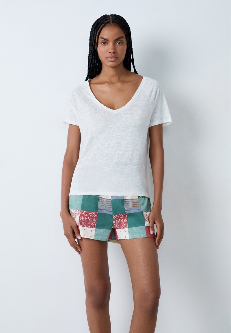 Camiseta blanca de manga corta y cuello en V combinada con pantalones cortos de patchwork en colores variados que incluyen tonos rojos, verdes y beiges.