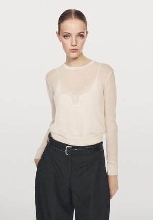 Haut léger et transparent à manches longues en blanc cassé, avec un col rond. Associé à un pantalon taille haute noir et une ceinture tressée noire.