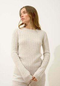 Jasnobeżowy sweter z prążkowanej tkaniny, wykonany z miękkiego, strukturalnego materiału, z długimi rękawami i okrągłym dekoltem, o dopasowanym kroju.