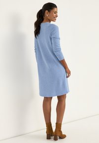 Blaues gestricktes Kleid mit langen Ärmeln und lockerem Schnitt, mit Rippenstruktur und rundem Halsausschnitt, kombiniert mit braunen Stiefeletten.