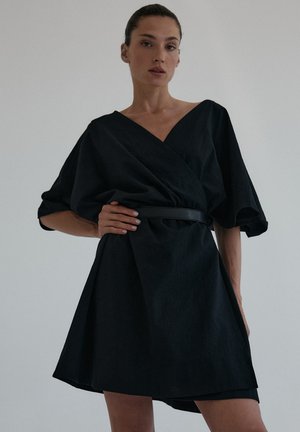 Czarna sukienka w stylu wrap z krótkimi, bufiaste rękawami i głębokim dekoltem w kształcie V. Posiada zawiązywany pas i rozkloszowany dół, wykonana z teksturowanej tkaniny.