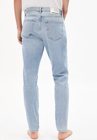 Jasnoniebieskie dżinsy z denimu o prostym kroju nogawki, wyposażone w dwie tylne kieszenie, widoczne szwy oraz metkę na pasku w talii.