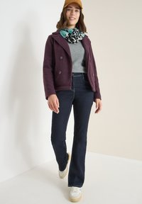 Purple textured double-breasted jacket, gray ribbed sweater, dark blue flared jeans, patterned scarf, light sneakers with cream soles.