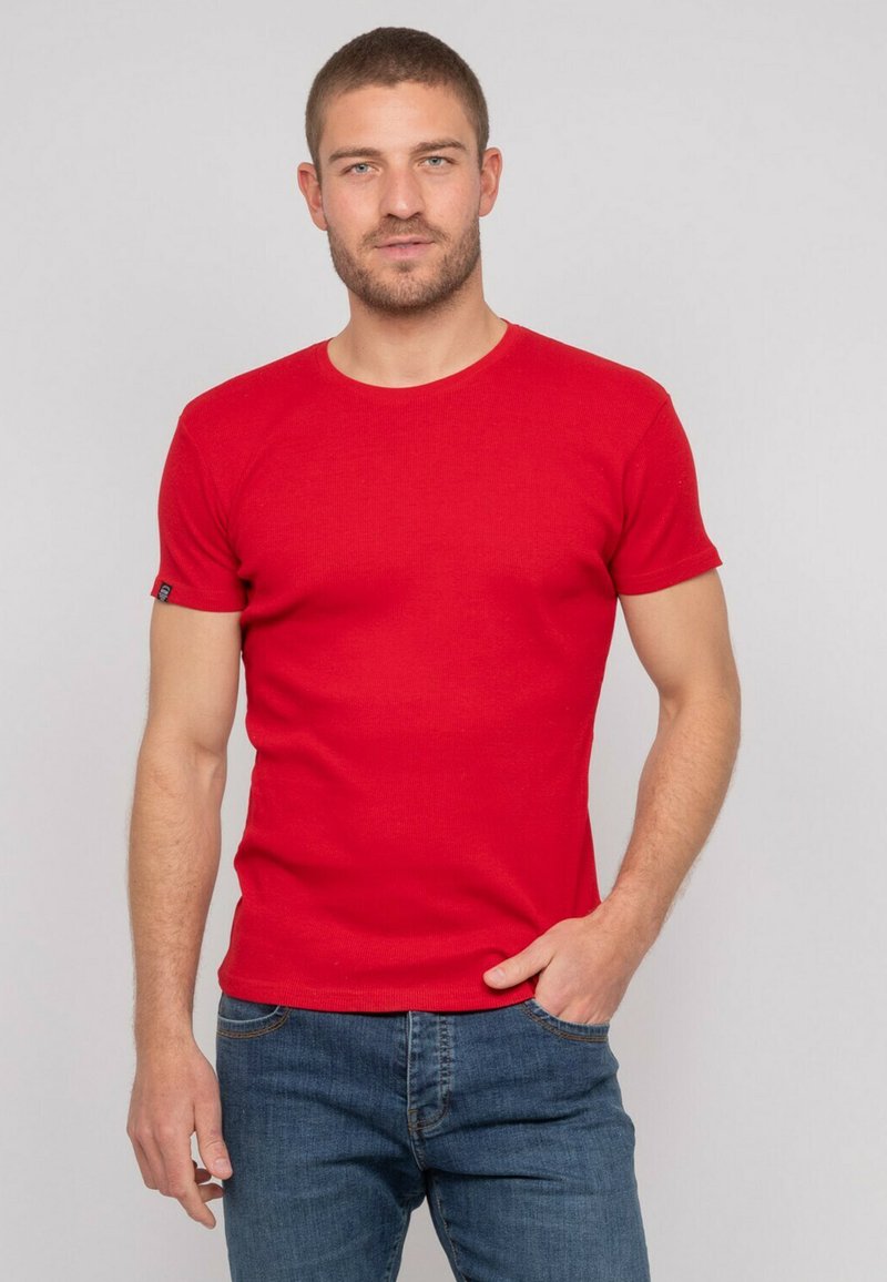 T-shirt rouge à manches courtes avec un col rond, fabriquée en tissu côtelé. Surface texturée et petite étiquette logo sur la manche gauche.