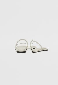 Flate sandaler med et lys grått gummibelte, med tynne stropper og kvadratisk tådesign, satt på en svart såle for kontrast.