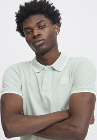 Polo shirt verde chiaro con tessuto texturizzato, colletto e accentature delle maniche bianche, con un logo discreto sul petto.