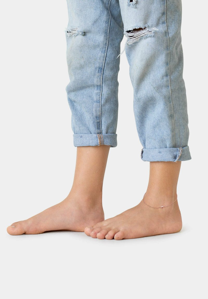 Lyseblå distressed denim jeans med opkrøllede manchetter, der afslører bare fødder. Anklen prydet med et delikat kædearmbånd.