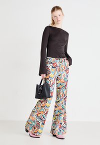 Maglietta nera a maniche lunghe abbinata a pantaloni svasati multicolori con un motivo a vortice. Il modello tiene una piccola borsa nera. Scarpe con tacco rosa.