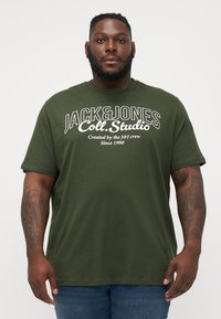 Olive green cotton t-shirt featuring a white printed logo and text on the front. Short sleeves and a relaxed fit. Plain background.