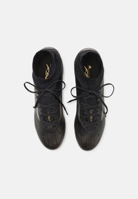 Black athletic shoes with a sleek design, featuring textured patterns, a sock-like fit, black laces, and gold accents on the tongue.