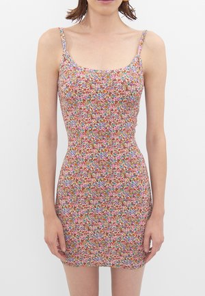 Kobieta ubrana w dopasowaną, bezrękawnikową mini sukienkę z cienkimi ramiączkami i małym, wielokolorowym kwiatowym wzorem na białym tle.