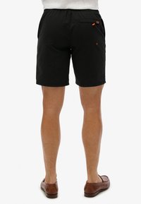 Pantaloni corti neri con vita elasticizzata, tasche laterali e una tasca posteriore con inserti arancioni. Materiale liscio e leggero.