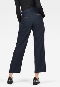 Marinblå vida byxor tillverkade av ett slätt material med rak skärning. Har två bakfickor med horisontella ränder och en skräddarsydd midja.