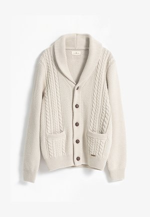 Suéter color crema con cuello tipo chal, con trenzados y patrones texturizados. Cuatro botones marrones y dos bolsillos delanteros.