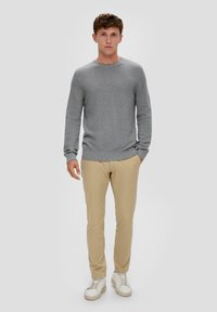 Pull en tricot gris avec un col rond, associé à un pantalon ajusté beige clair et des baskets blanches. Design de tissu simple et texturé.