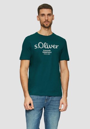 Teal Baumwoll-T-Shirt mit Rundhalsausschnitt, versehen mit einem weißen Logo und Textdesign. Kombiniert mit blauen Jeans. Kurze Ärmel, lässige Passform.