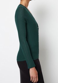 Vihreä ribbineuloinen neuletakki, jossa pitkät hihat ja V-pääntie, etupuolella napit ja hieman kapeneva helma. Pehmeä pinta ja pystysuorat linjat.