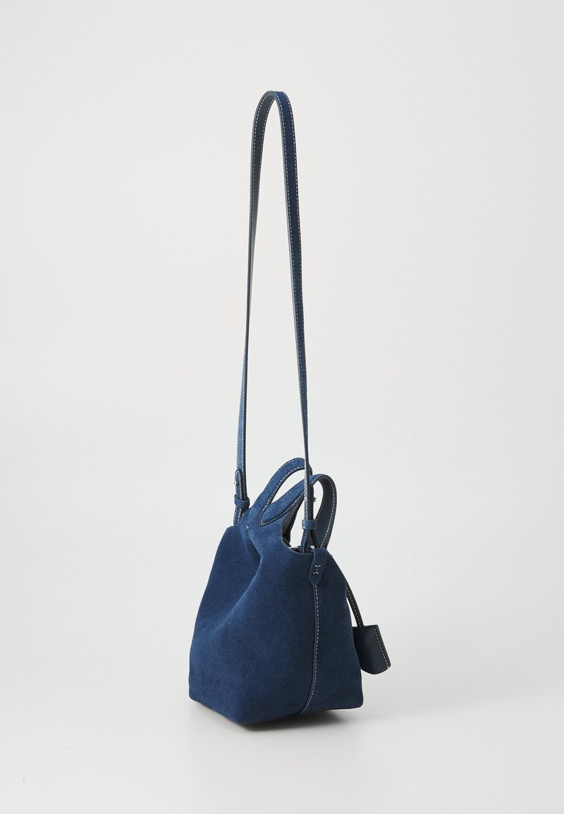 Žydros suedenos rankinė, su struktūrine forma, dviem viršutinėmis rankenomis ir ilgu, reguliuojamu diržu. Yra kontrastingi siūlai ir šoninė etiketė.