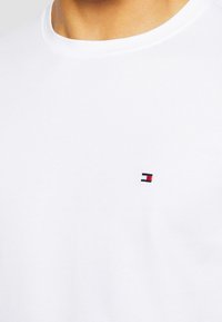 White short-sleeve T-shirt made of cotton, featuring a small, embroidered logo in red, white, and blue on the left chest area.