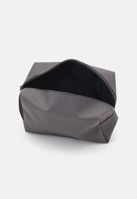 Rektangulær kosmetikkveske i glatt, mørkegrått materiale. Den har en glidelås på toppen og myk innside, med fleksible sider for enkel tilgang.
