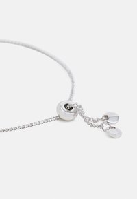 Silverfärgad kedjebracelet med ett runt spänne, med två små platta hängen hängande från en dubbelkedja. Slät, glänsande yta.