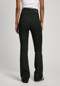 Pantalones vaqueros de campana negros con una cintura alta y dos bolsillos traseros. La tela es suave con un ligero estiramiento. Presenta una etiqueta de marca en la cintura.