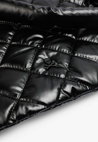Chaqueta acolchada negra con un diseño de diamantes, fabricada con material brillante, y un pequeño emblema de calavera y huesos cruzados.