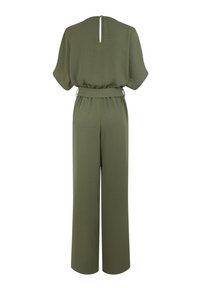 Combinaison vert olive en tissu texturé, à manches courtes et avec une ceinture à la taille. Présente une ouverture en forme de clé au dos et un design à jambes larges.
