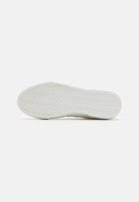 Shoe outsole in white rubber with a herringbone pattern. Features smooth edges and a flat shape, designed for traction and durability.