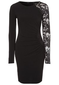 Zwarte jurk met lange mouwen; één mouw heeft kantdetails. Bodycon pasvorm met geplooide textuur aan één kant, ronde halslijn.