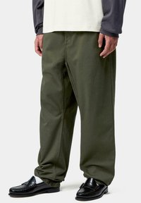 Persona con pantalones holgados verde oliva, mocasines de cuero negros, calcetines blancos y una camiseta de manga larga en capas con mangas blancas y gris oscuro.