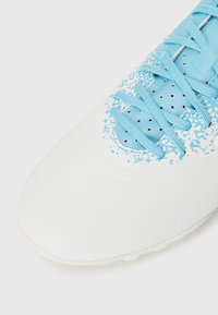 White soccer shoe with a smooth finish, featuring light blue accents and textured overlay. Blue laces and perforated areas for ventilation.